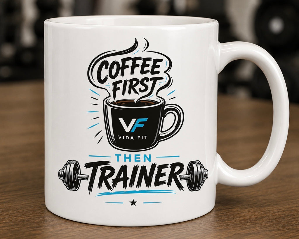 Coffee First Then Trainer white ceramic mug with Vida Fit logo on wooden surface