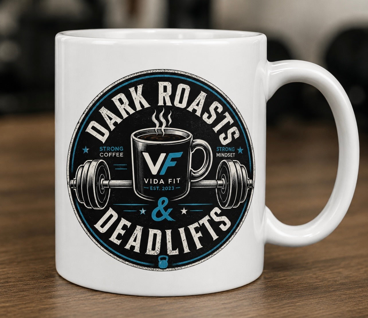 Dark Roasts & Deadlifts white ceramic mug with Vida Fit logo on wooden surface